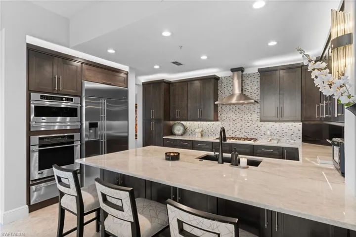 Kitchen with a peninsula, light stone countertops, a breakfast bar, dark wood finish cabinetry, and stainless steel double oven