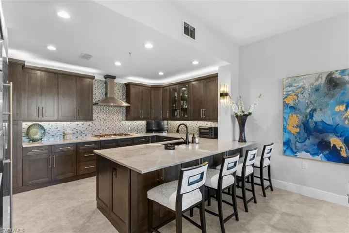 Kitchen with glass insert cabinets, dark wood finish cabinetry, a breakfast bar, a peninsula, and light stone counters