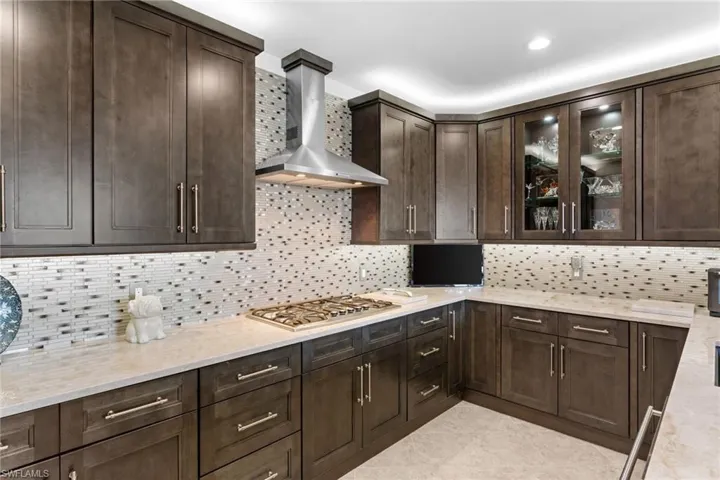 Kitchen with dark wood finish cabinetry, light stone counters, tasteful backsplash, stainless steel gas stovetop, and light tile patterned floors
