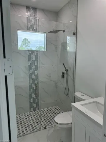 Bathroom featuring tiled shower, tile patterned floors, toilet, and vanity