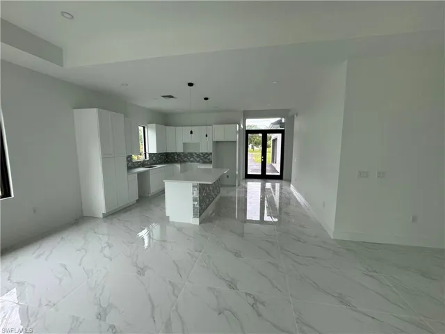 Kitchen with sink, light tile patterned floors, a kitchen island, decorative backsplash, and white cabinetry