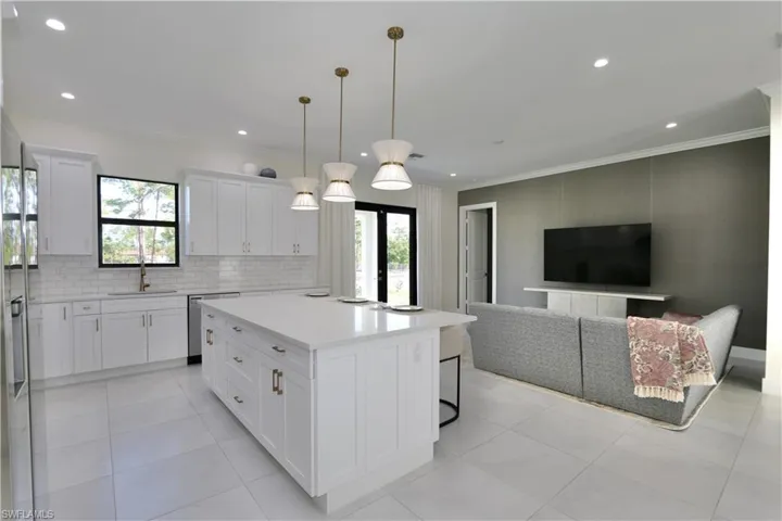 Kitchen featuring open floor plan, white cabinets, a center island with sink, pendant lighting, and a kitchen bar