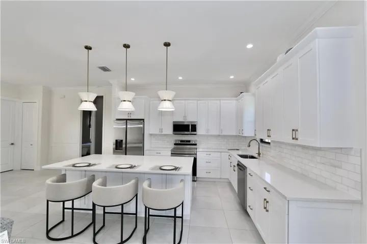 Kitchen featuring stainless steel appliances, crown molding, white cabinetry, a kitchen bar, and a center island