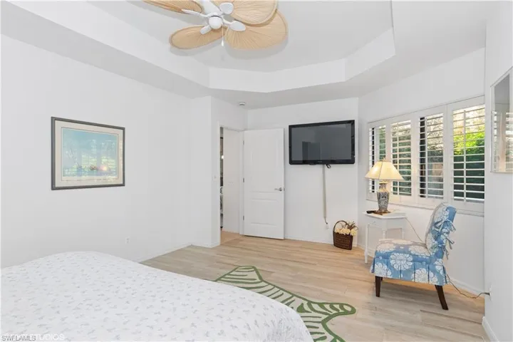Bedroom featuring light wood finished floors, ceiling fan, baseboards, and a raised ceiling