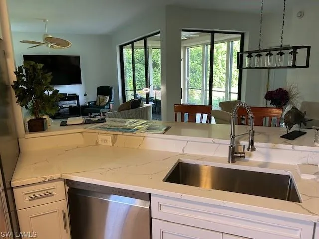 Kitchen with open floor plan, stainless steel dishwasher, white cabinetry, light stone counters, and ceiling fan