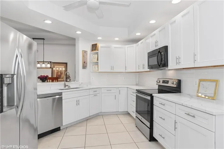 Kitchen featuring a tray ceiling, light tile patterned floors, open shelves, appliances with stainless steel finishes, and a sink