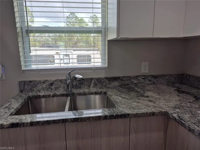 Kitchen with stone counters, sink, and white cabinets