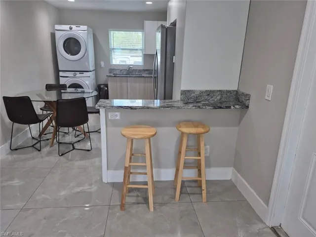 Kitchen with dark stone countertops, stainless steel fridge, white cabinets, stacked washer and dryer, and kitchen peninsula