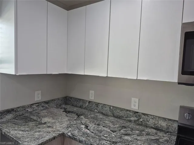 Details with range with electric stovetop, white cabinets, and dark stone counters