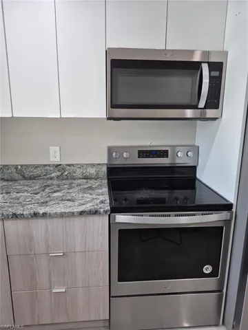 Kitchen with appliances with stainless steel finishes, stone countertops, and white cabinets