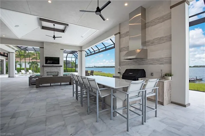 View of patio with ceiling fan, a tiled fireplace, area for grilling, a water view, and exterior bar