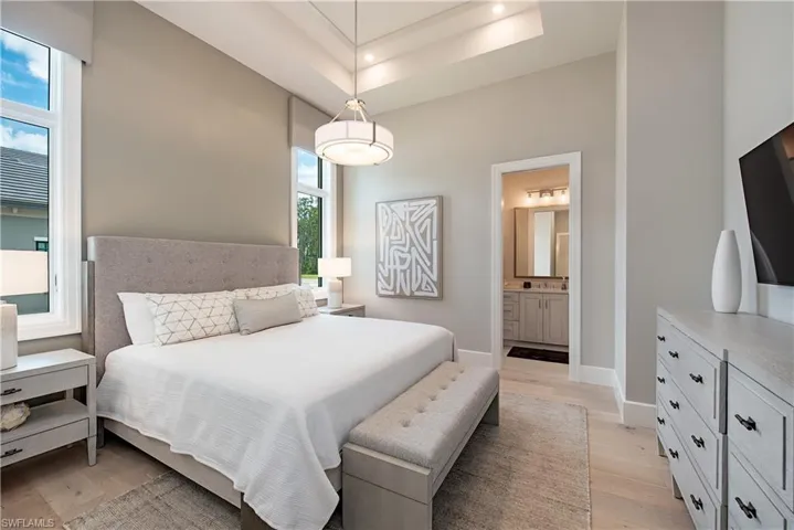 Bedroom featuring light wood-style floors, a raised ceiling, ensuite bathroom, and baseboards