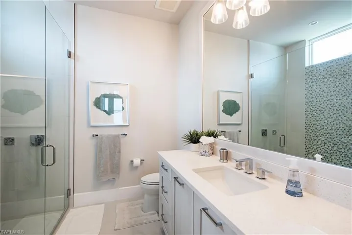 Bathroom featuring an inviting chandelier, vanity, toilet, baseboards, and a stall shower