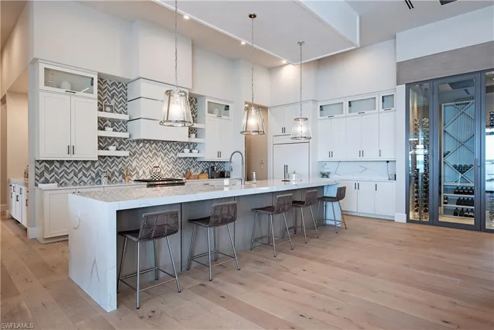 Kitchen featuring decorative backsplash, a towering ceiling, open shelves, a spacious island, and light wood-type flooring