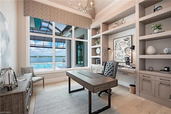 Office featuring an inviting chandelier, built in study area, light wood-type flooring, a water view, and built in shelves