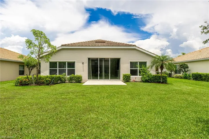 Rear view of house with stucco siding, a yard, a tile roof, and a patio