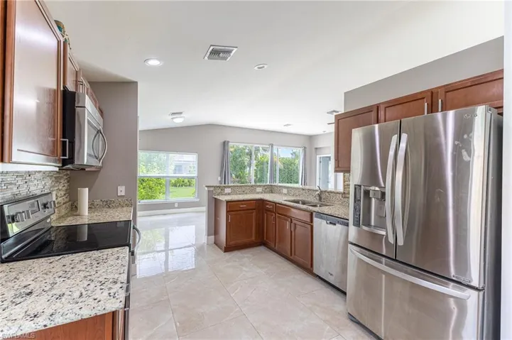 Kitchen with appliances with stainless steel finishes, a peninsula, lofted ceiling, light stone counters, and brown cabinetry