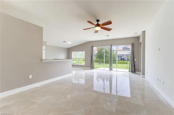 Empty room featuring light marble finish floors, ceiling fan, and vaulted ceiling