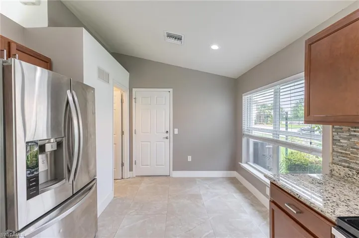 Kitchen featuring stainless steel refrigerator with ice dispenser, lofted ceiling, recessed lighting, brown cabinetry, and light stone counters