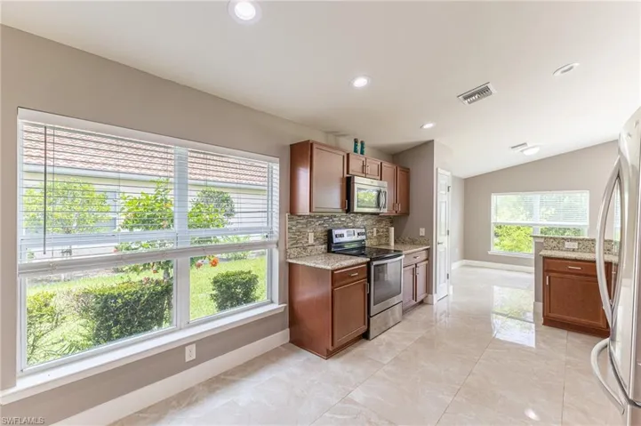 Kitchen featuring appliances with stainless steel finishes, vaulted ceiling, tasteful backsplash, light stone counters, and recessed lighting