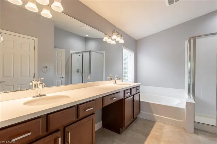 Bathroom featuring a shower stall, double vanity, a garden tub, tile patterned flooring, and vaulted ceiling
