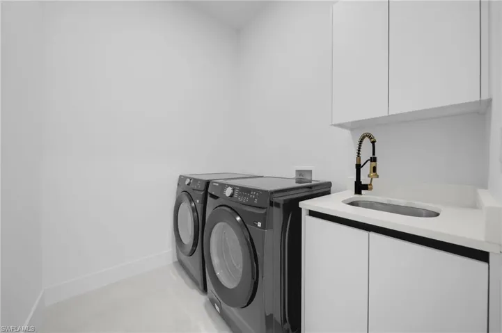 Laundry area featuring cabinet space, washer and clothes dryer, baseboards, and a sink