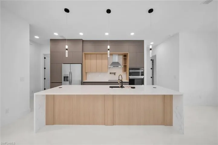 Kitchen featuring stainless steel fridge, modern cabinets, a sink, wall chimney range hood, and decorative backsplash
