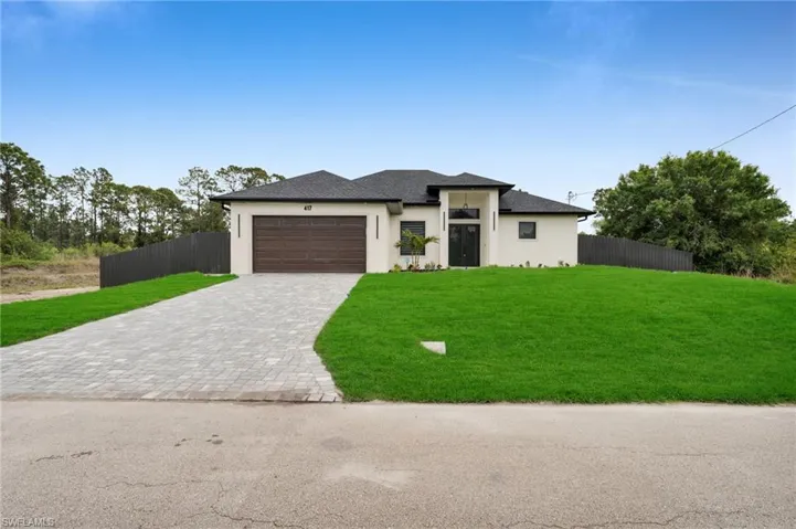 Prairie-style house with an attached garage, fence, stucco siding, a front lawn, and decorative driveway