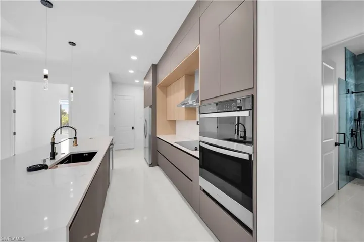 Kitchen with wall chimney exhaust hood, modern cabinets, appliances with stainless steel finishes, a sink, and gray cabinetry
