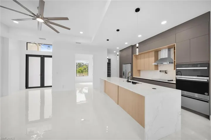 Kitchen featuring stainless steel fridge with ice dispenser, modern cabinets, wall chimney range hood, a tray ceiling, and black electric stovetop