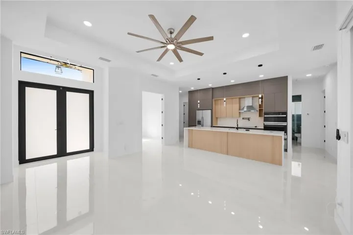 Kitchen featuring wall chimney range hood, a tray ceiling, modern cabinets, and stainless steel refrigerator with ice dispenser