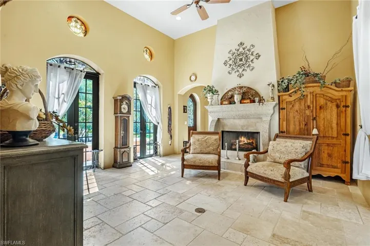 Sitting room with stone tile floors, a high ceiling, a large fireplace, arched walkways, and ceiling fan