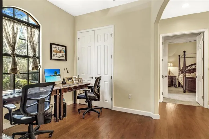 Home office featuring arched walkways, dark wood-style floors, and baseboards