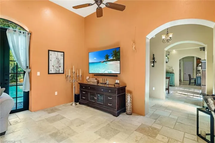 Living room featuring ceiling fan with notable chandelier, arched walkways, and stone tile floors