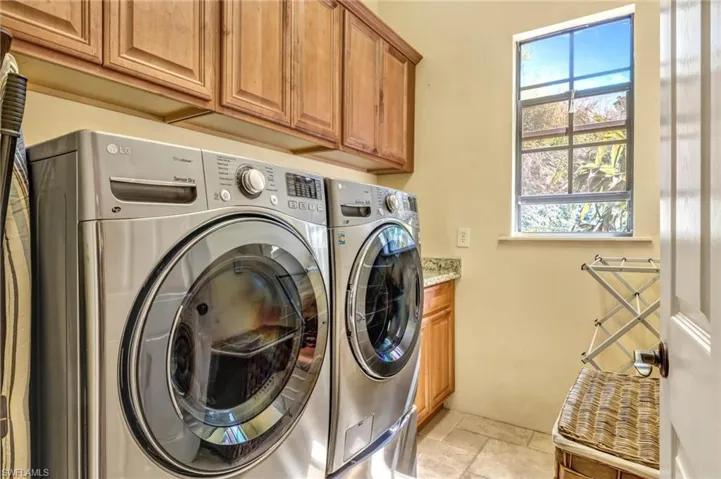 Laundry area featuring washing machine and dryer, cabinet space, stone tile flooring, and a healthy amount of sunlight
