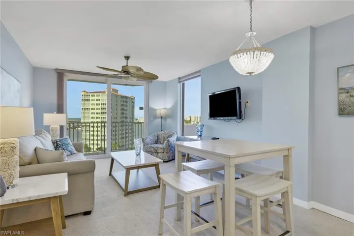 Living area with floor to ceiling windows, light colored carpet, a ceiling fan, and a chandelier