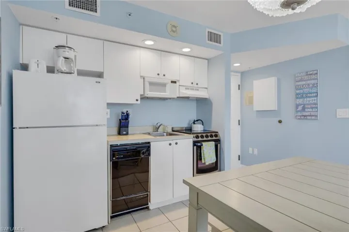 Kitchen with white appliances, white cabinets, light countertops, under cabinet range hood, and recessed lighting