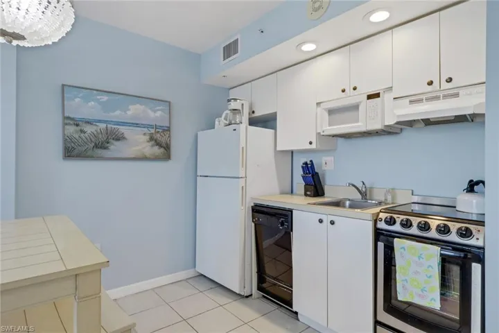 Kitchen with white appliances, white cabinets, light countertops, and under cabinet range hood