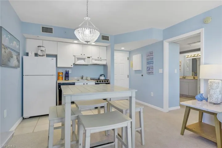 Kitchen with white appliances, white cabinets, light countertops, light colored carpet, and a chandelier