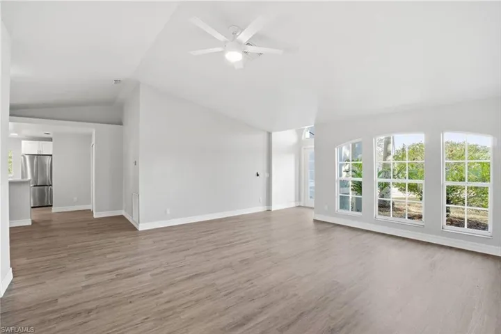 Unfurnished living room featuring plenty of natural light, light wood finished floors, lofted ceiling, and ceiling fan