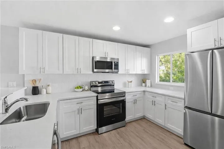 Kitchen with appliances with stainless steel finishes, white cabinets, recessed lighting, light stone countertops, and light wood finished floors