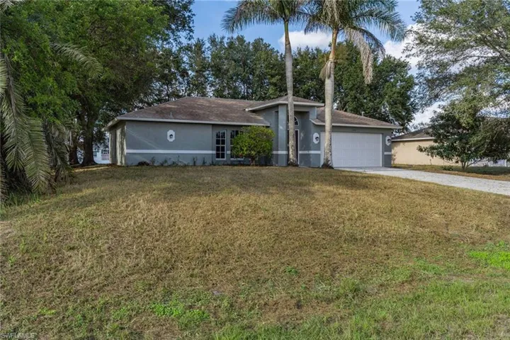 Ranch-style home with stucco siding, driveway, a front lawn, and an attached garage