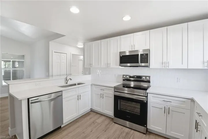 Kitchen with appliances with stainless steel finishes, a peninsula, white cabinets, light wood-style floors, and backsplash