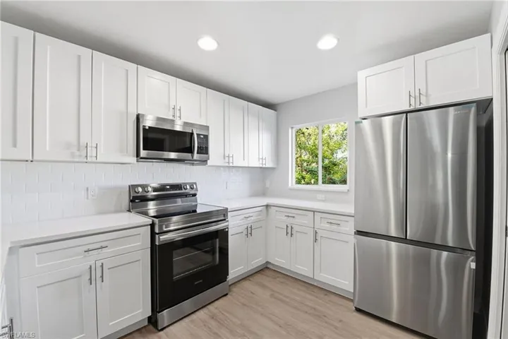 Kitchen with appliances with stainless steel finishes, white cabinets, light wood-type flooring, decorative backsplash, and recessed lighting