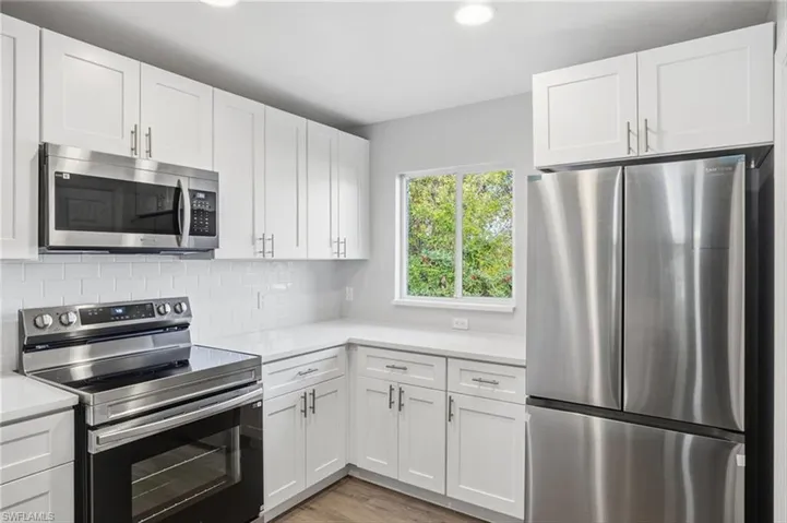 Kitchen featuring appliances with stainless steel finishes, white cabinetry, decorative backsplash, light wood-type flooring, and recessed lighting