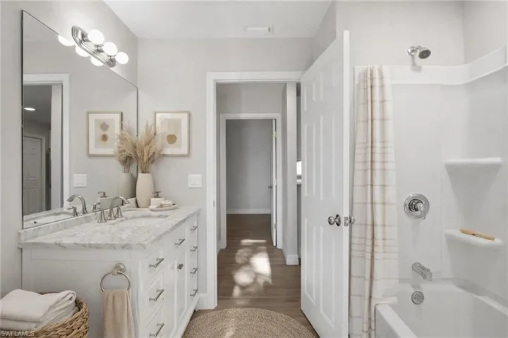 Full bath featuring vanity, shower / bathtub combination with curtain, and dark wood finished floors