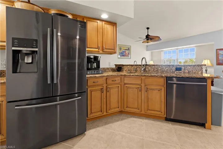 Kitchen featuring stone counters, sink, ceiling fan, light tile patterned floors, and appliances with stainless steel finishes