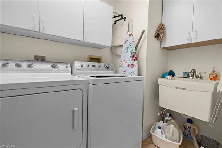 Washroom with washer and clothes dryer, light tile patterned flooring, cabinets, and sink