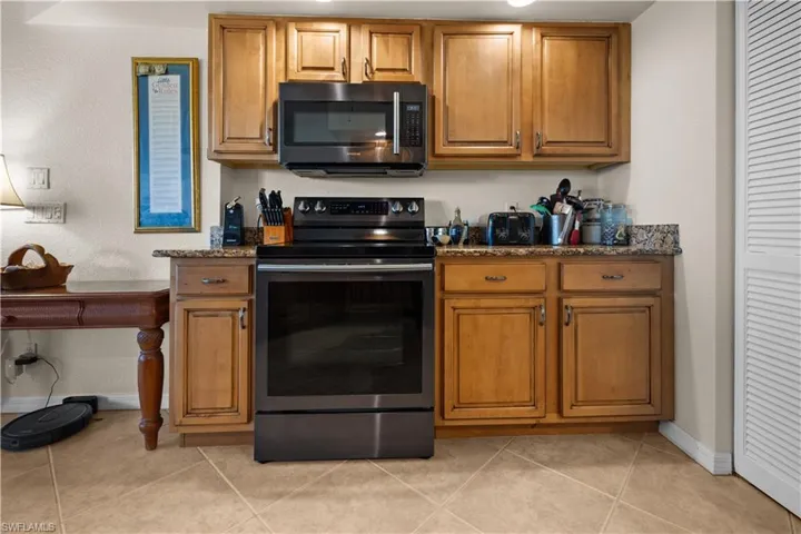 Kitchen with black range with electric stovetop, light tile patterned flooring, and dark stone counters