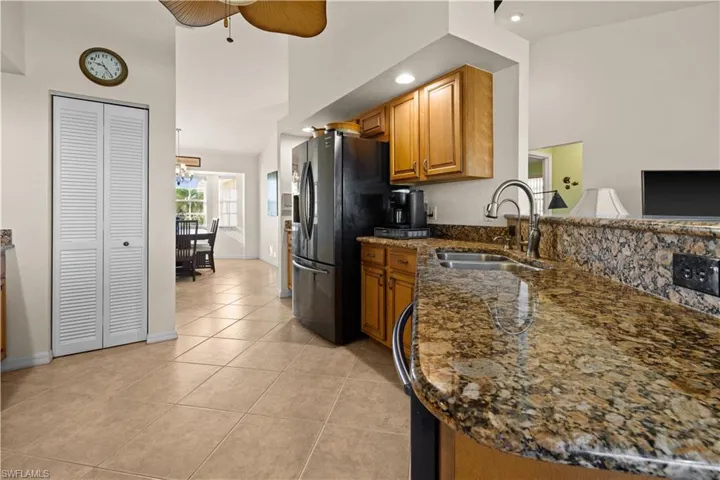 Kitchen with high vaulted ceiling, sink, dark stone countertops, light tile patterned flooring, and kitchen peninsula